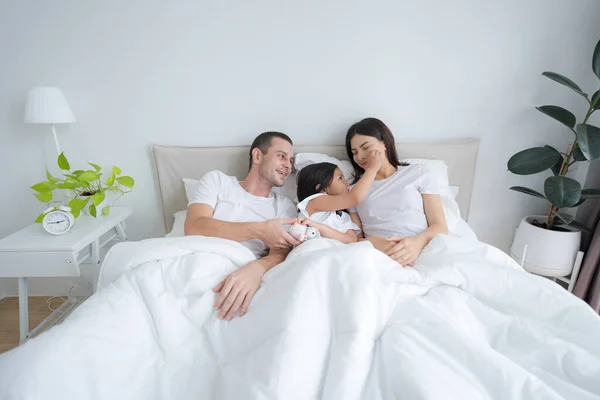 素敵な両親と娘の幸せな笑顔が快適な白いベッドの中でラウンジ — ストック写真