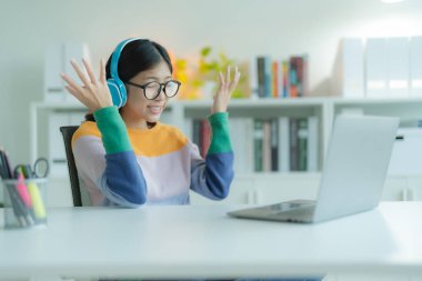 Kütüphanede dizüstü bilgisayar kullanan genç bir kadın ya da öğrenci gözlük ve kulaklık takıyor. Gülümsüyor ve mutlu görünüyor..