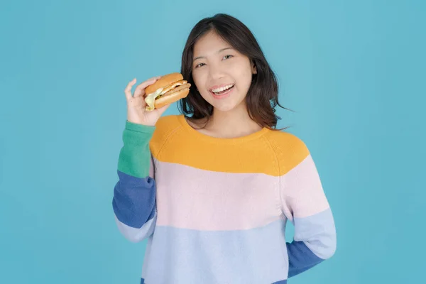 Piękna Młoda Kobieta Uśmiecha Się Szczęśliwie Trzymając Hamburgera Dłoni Niebieskim — Zdjęcie stockowe
