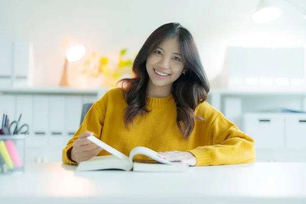 一个年轻的女人或学生戴着眼镜在图书馆看书 她面带微笑 看上去很快乐 — 图库照片