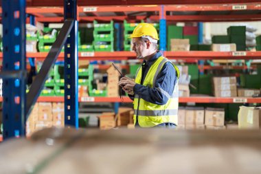 Depoda radyo kullanan bir erkek çalışan müşterilerin ihtiyaçlarını karşılamak için ürünü denetliyor..