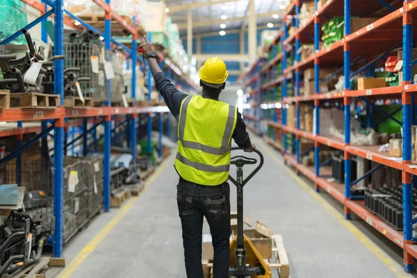 Male clerk pushing a cart or picking cart to organize items in a warehouse with warehouse goods background.