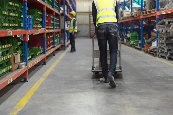 Male clerk pushing a cart or picking cart to organize items in a warehouse with warehouse goods background.