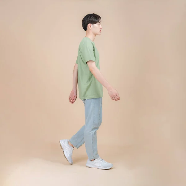 ベージュの背景にスタジオに立つ緑のTシャツとジーンズの男性ファッションモデル 流行の服スタイル コピースペース — ストック写真