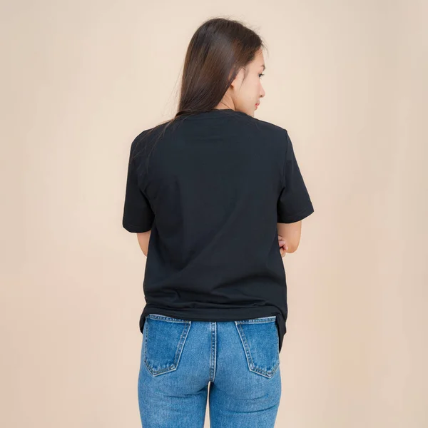 穿着黑色T恤和牛仔裤的女模特站在工作室里 穿着米色背景 时尚服装风格 复制空间 — 图库照片