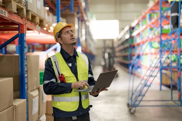 Male factory manager standing laptop to inspect the products in the warehouse while looking at the products on the shelves