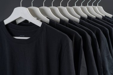 Askılardaki siyah tişörtlerin yakın çekimi, siyah tişörtlerden oluşan bir kolleksiyon, ahşap bir elbise askısı, giysi arka planı.