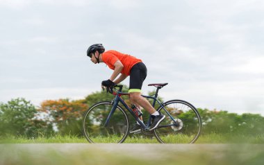 Spor kıyafetleri giyen genç bir adam, güneşli bir günde bisiklet süren bir bisikletçi açık havada bisiklet süren, siyah bisiklette spor yapan bir adam.