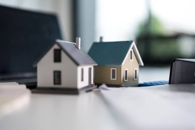 Dizüstü bilgisayar, hesap makinesi, planlar ve renk örnekleri yanında minyatür evler, emlak planlamasını sembolize ediyor