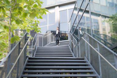 Profesyonel takım elbiseli kadın modern bir ofis binasının merdivenlerinden aşağı iniyor.