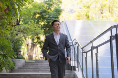 Zarif iş kıyafetleri içinde kendine güvenen genç bir işadamı şehir merkezinde güvenli bir şekilde yürüyor. Güneşli bir günde azim ve motivasyonla merdivenlerden çıkmak