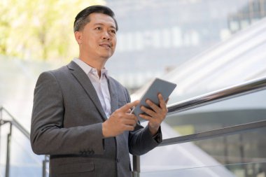 Takım elbiseli profesyonel bir adam elinde tabletle dışarıda duruyor. Uzağa dikkatlice bakıyor.