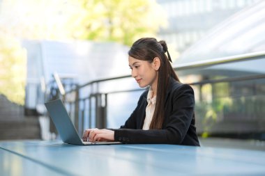 Odaklanmış iş kadını, modern bir açık hava ortamında dizüstü bilgisayarıyla çalışıyor.