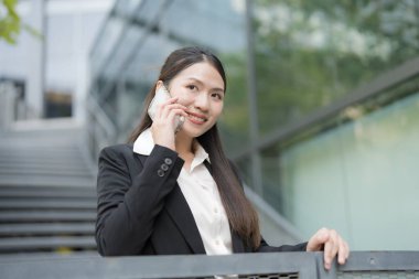 Şehrin balkonunda akıllı telefon kullanan gülümseyen profesyonel bir kadın.