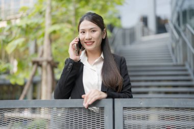 Şehrin balkonunda akıllı telefon kullanan gülümseyen profesyonel bir kadın.