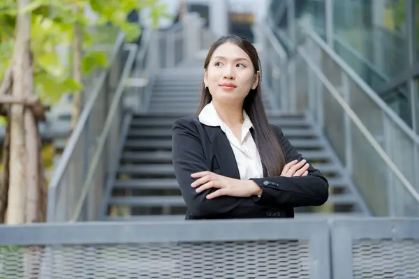 Young asian professional businesswoman smiling confidently in an urban environment. Wearing modern business attire. Showcasing elegance and positivity. In front of an office building staircase