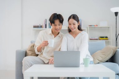 Genç çift, modern ve birbirine bağlı bir yaşam tarzını yansıtan parlak, rahat oturma odalarında dizüstü bilgisayarlarında içeriklerini keşfetmekten zevk alıyor.