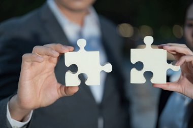 Büyük yapboz parçaları tutan iki profesyonelin yakın plan görüntüsü, işbirliği, problem çözme ve ortak bir amaca doğru ortaklığı temsil ediyor.