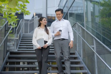İki profesyonel, elinde bir tabletle bir ofis binasının merdivenlerinde sohbet ediyorlar.