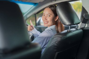 Sürücü koltuğunda oturan gülümseyen genç bir kadın, güvenli ve eğlenceli bir sürüş altını çizerek, parlak ve neşeli bir ifadeyle bir arabanın direksiyonunu kendinden emin bir şekilde tutuyor.