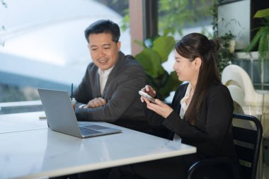 İki şirket ortağı, modern bir açık hava kafede dizüstü bilgisayar kullanarak iş birliği yapıyor.
