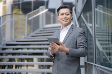 Ofis merdivenlerinde dijital tablet kullanan takım elbiseli, gülümseyen profesyonel bir adam.