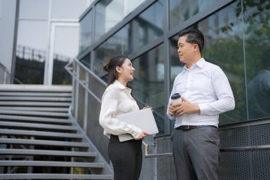 İki profesyonel, elinde bir tabletle bir ofis binasının merdivenlerinde sohbet ediyorlar.