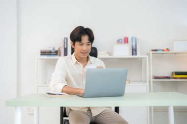 Genç bir adam, parlak, modern bir ofis ortamında dizüstü bilgisayarda bir fincan kahve ve rahat bir sandalyeyle uzaktan kumandalı çalışmanın örneğini veriyor.