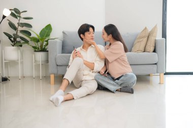 Sevgi dolu bir çift yerde oturuyor, şefkatli bir bakış ve nazik bir dokunuş, parlak ve modern oturma odalarında samimi bir an yaratıyor.