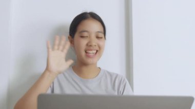 Dizüstü bilgisayarıyla video görüşmesi yapan genç bir kadın elleriyle hareket ederken hareketli bir şekilde konuşuyor. Dekor, doğal ışık alan rahat bir ofis ortamı içeriyor.