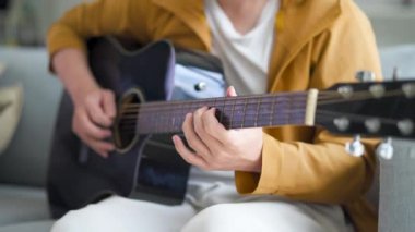 Genç adam rahat bir şekilde rahat bir oturma odasında kanepede oturur, akustik gitar çalar. Atmosfer, müzik için rahatlama ve tutku yayıyor. Yeteneğini ve yaratıcılığını gösteriyor.