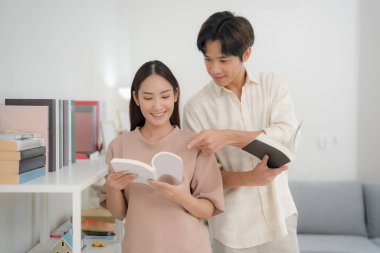 Genç, neşeli bir çift, arka planda edebiyat seçimiyle sakin bir sevinç anını paylaşmak için, iyi aydınlatılmış bir odada kitap okuyor.