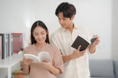 Genç, neşeli bir çift, arka planda edebiyat seçimiyle sakin bir sevinç anını paylaşmak için, iyi aydınlatılmış bir odada kitap okuyor.