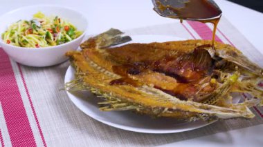 Şef, kızarmış balığın üzerine lezzetli bir sos döker, canlı bir mango salatasıyla birlikte servis edilir, ve nefis bir aşçılık deneyimi yaratır.