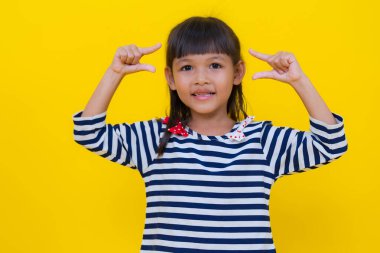 Gülümseyen Asyalı genç bir kızın stüdyo portresi canlı sarı bir arkaplan karşısında duruyor, kolları güven içinde kesişiyor, neşe ve kendine güven duygusu yayıyor.