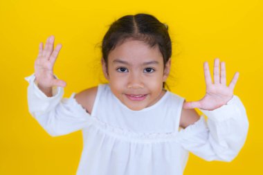 Şaşırmış Asyalı kız ağzını açıyor ve sarı arka planda ellerini kaldırıyor.