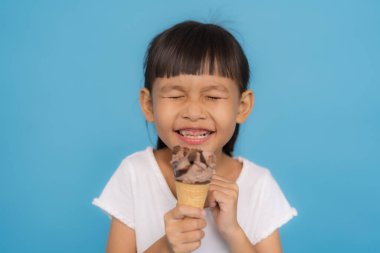 Mutlu çocuk lezzetli bir çikolatalı dondurma yiyor, canlı mavi bir arka planda tatlı bir ziyafetin tadını çıkarıyor, yaz ve çocukluk keyfi kavramları için mükemmel.