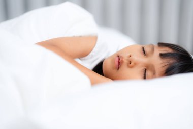 Asyalı çocuk rahat beyaz bir yatakta uyur, huzurlu bir uykudan zevk alır, çocukluk, dinlenme ve rahatlama kavramlarını temsil eder.