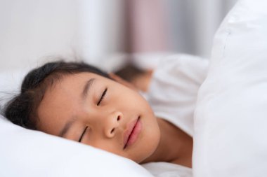 İki küçük Asyalı kız huzur içinde uyuyorlar ve beyaz battaniyenin altında el ele tutuşuyorlar. Dinlenme ve bağlanma anlarının tadını çıkarıyorlar.