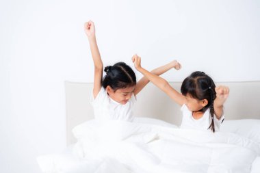 İki genç Asyalı kız kardeş uyanır ve yatağa uzanırlar, rahat beyaz bir battaniyeye sarınırlar, mutluluk ve enerji dolu yeni bir günün mutluluğunu kucaklarlar.