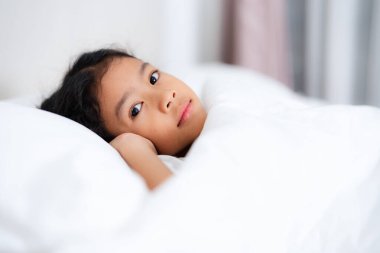 Asyalı çocuk rahat beyaz bir yatakta uyur, huzurlu bir uykudan zevk alır, çocukluk, dinlenme ve rahatlama kavramlarını temsil eder.