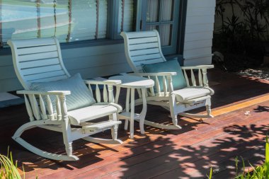 Cozy white rocking chairs on a sunny wooden porch. clipart