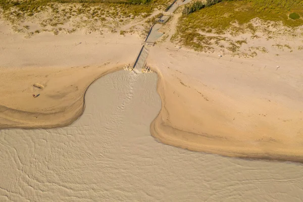 Drone photography of river ending in ocean dumping factory water during summer day.