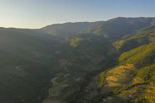 Drone photography of forested mountain side, farms and farmlands during summer evening