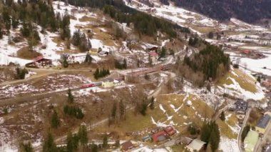 Drone video of mountain railway and train running on it through forest and houses