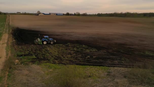 春の夕暮れ時に耕作場と農家の運転トラクターのドローン映像 高角度表示 — ストック動画