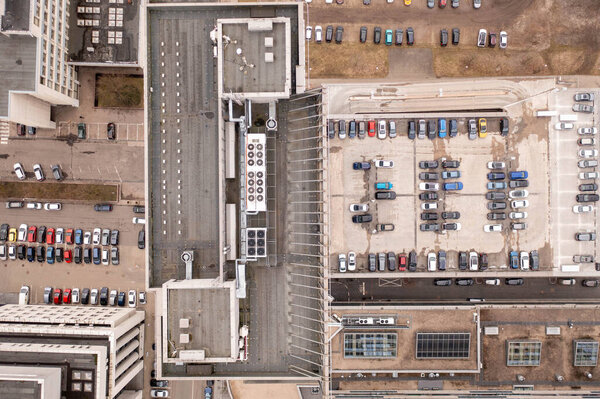 Drone photography of skyscraper rooftop and parking lot near skyscraper during spring cloudy day. Directly above
