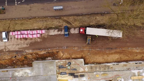 Drone photography of unloading semi truck with a forklift in a construction site during spring cloudy morning. Directly above