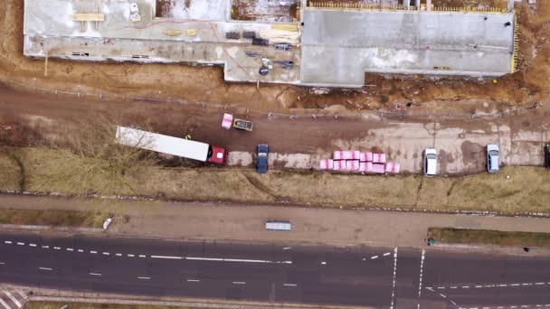 春の曇りの朝中に建設現場でフォークリフトで半トラックを積み降ろしのドローン映像 — ストック動画