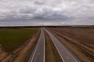 İlkbahar bulutlu bir günde kırsal alanda tarımsal alanlarla çevrili otobanın insansız hava aracı fotoğrafçılığı